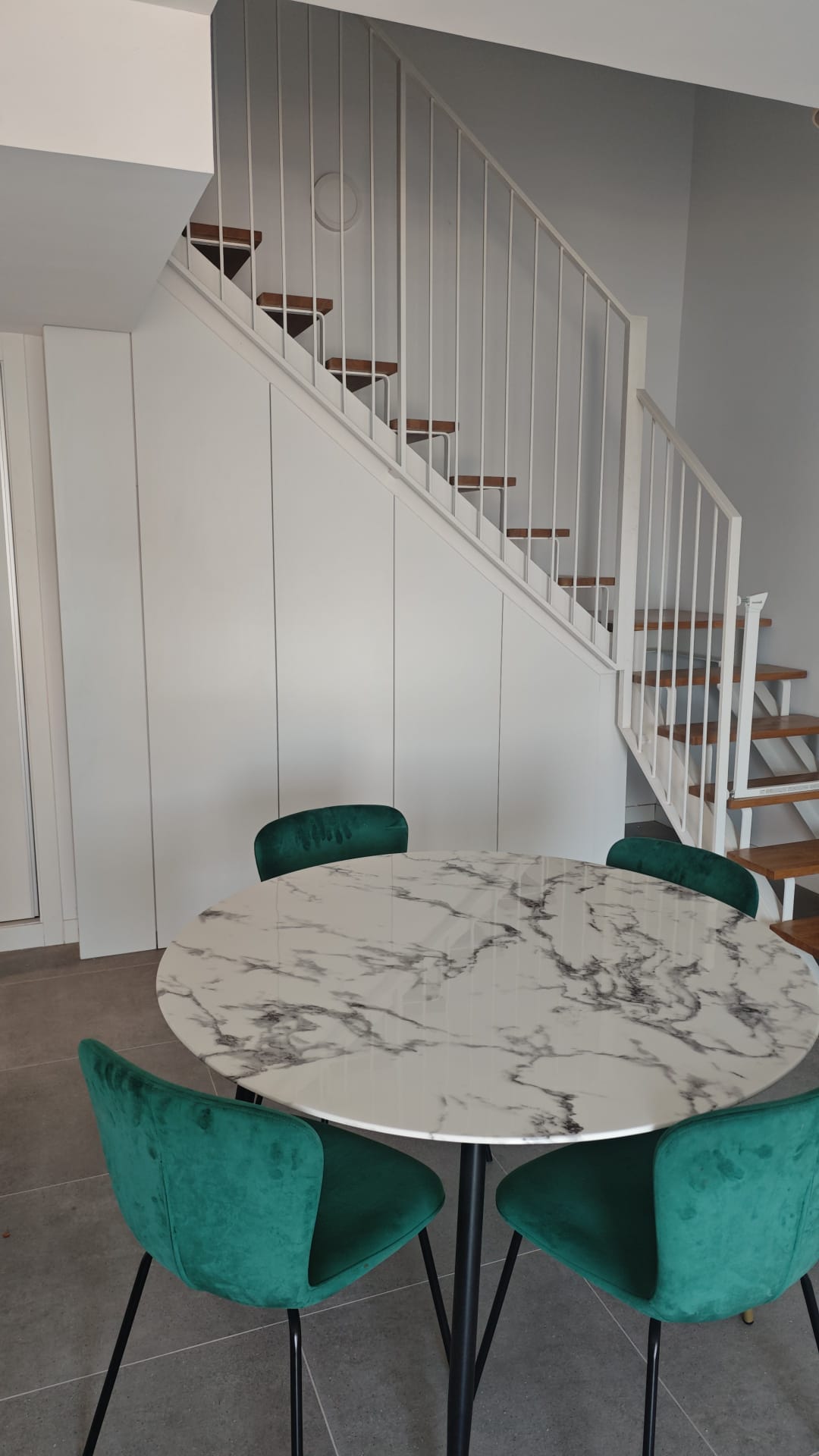 Comedor bajo escalera con mesa de mármol, sillas de terciopelo verde y carpintería lacada bajo la escalera