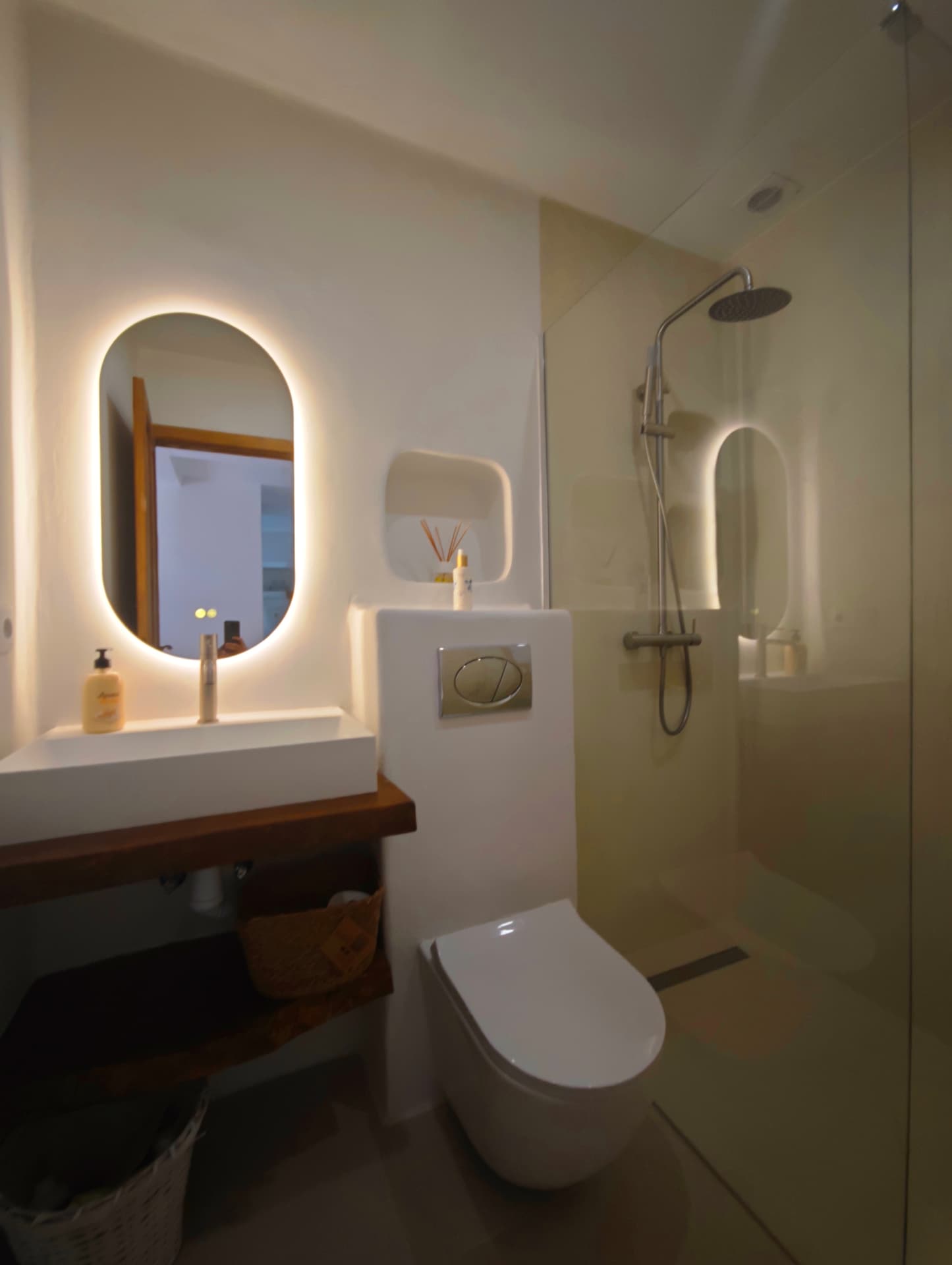 Baño en suite con espejo retroiluminado, inodoro suspendido y ducha con mampara de vidrio