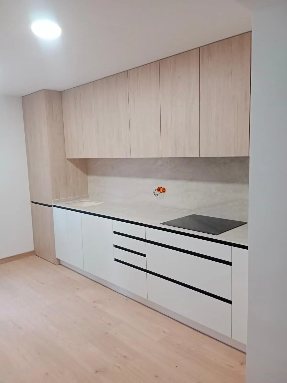 Cocina minimalista con módulos altos en roble claro, frentes blancos sin tirador y encimera de porcelánico