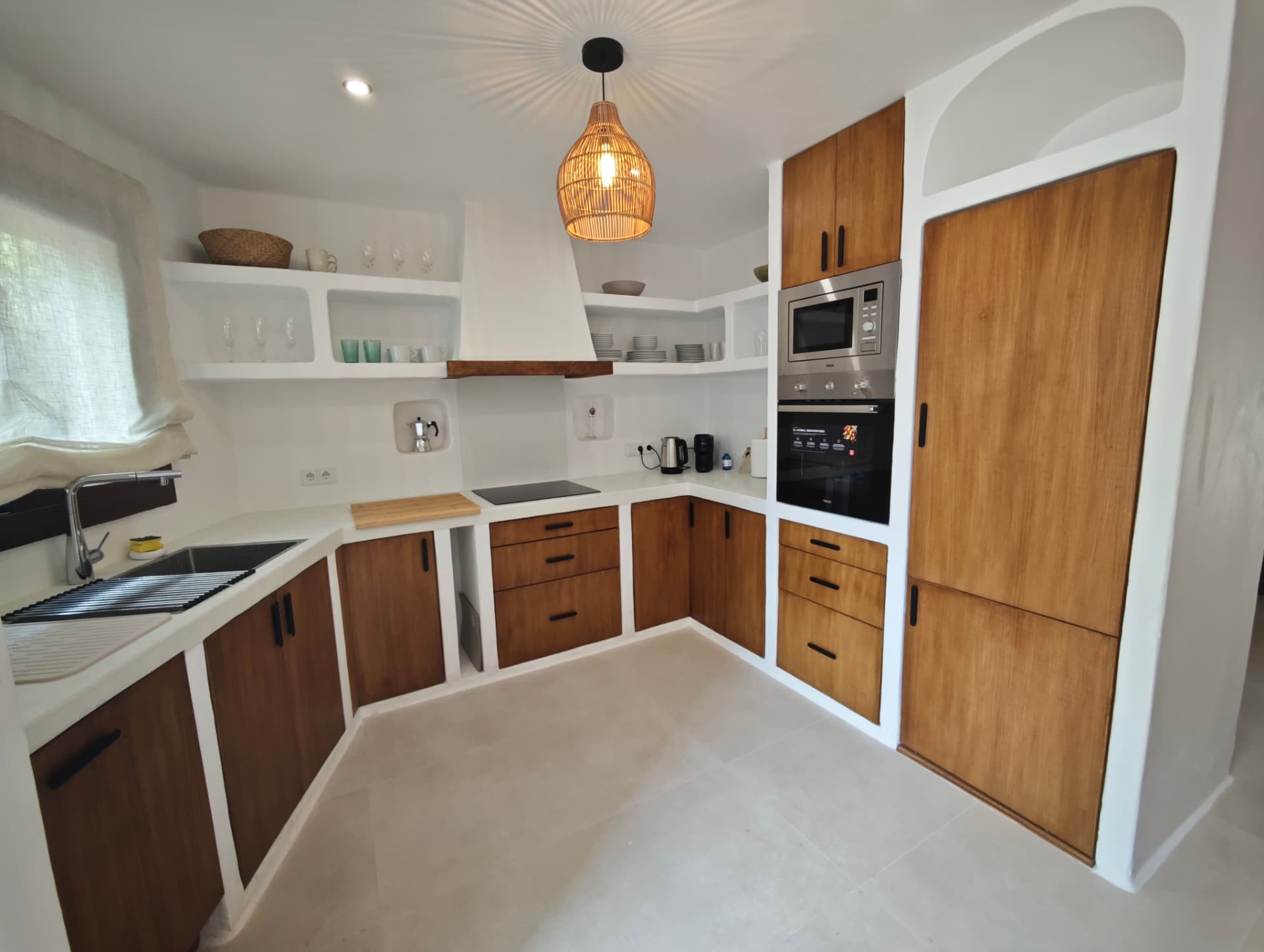 Cocina terminada en Jávea con armarios de obra de estilo ibicenco, encimera de microcemento y lámpara de mimbre