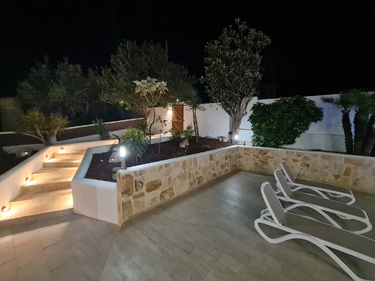 Patio exterior con muro de piedra natural, jardinera de obra e iluminación nocturna