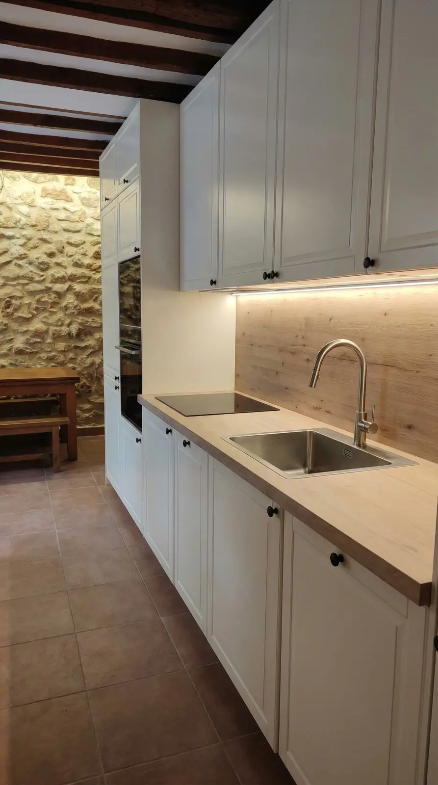Cocina clásica en blanco con encimera de madera, vigas vistas y pared de piedra natural